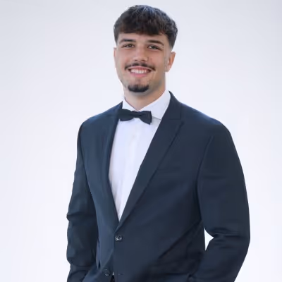 Young man in a black tuxedo with bow tie smiling against a plain white background.
