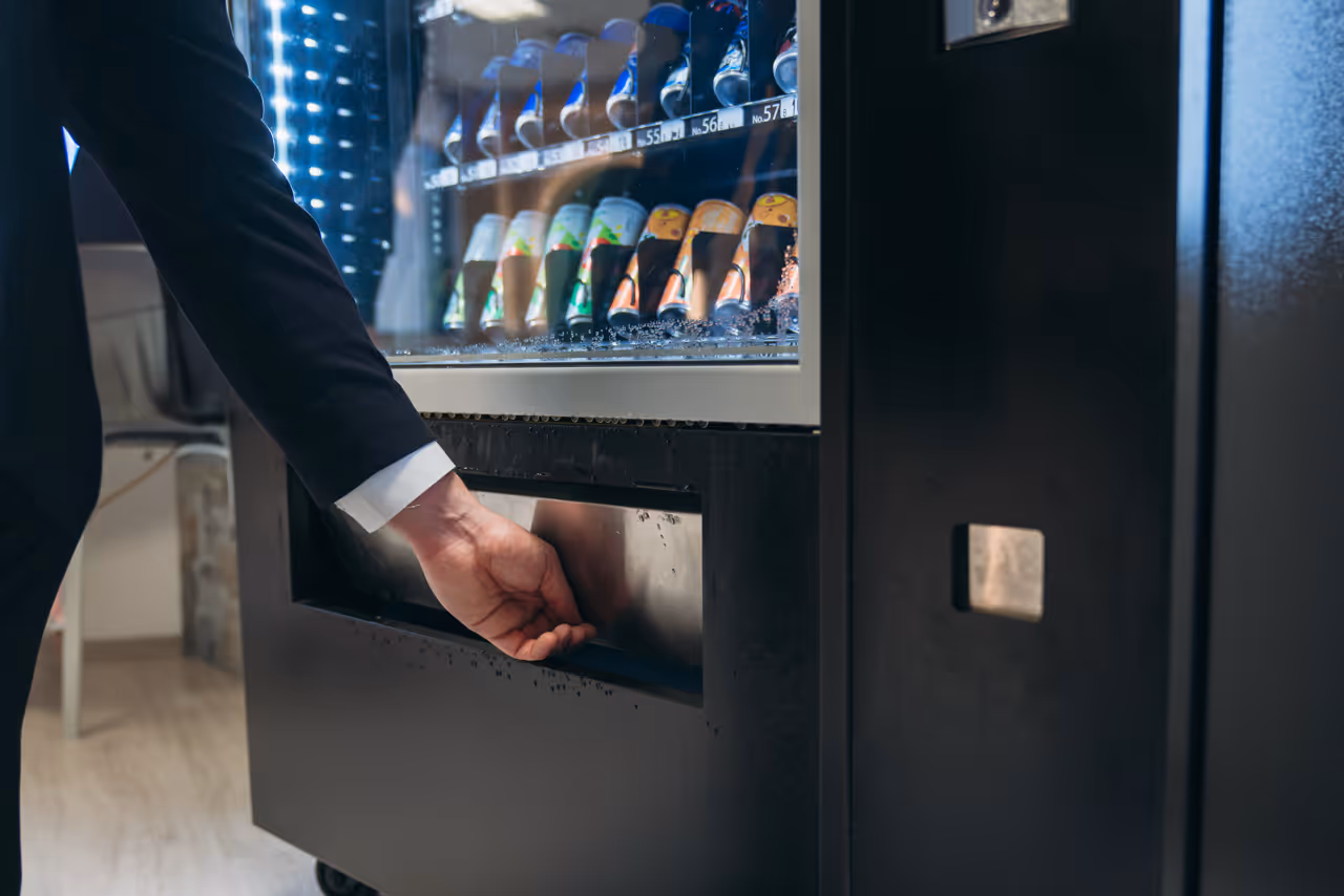 Man's hand in suit collecting a beverage bottle from a vending machine's dispensing area.