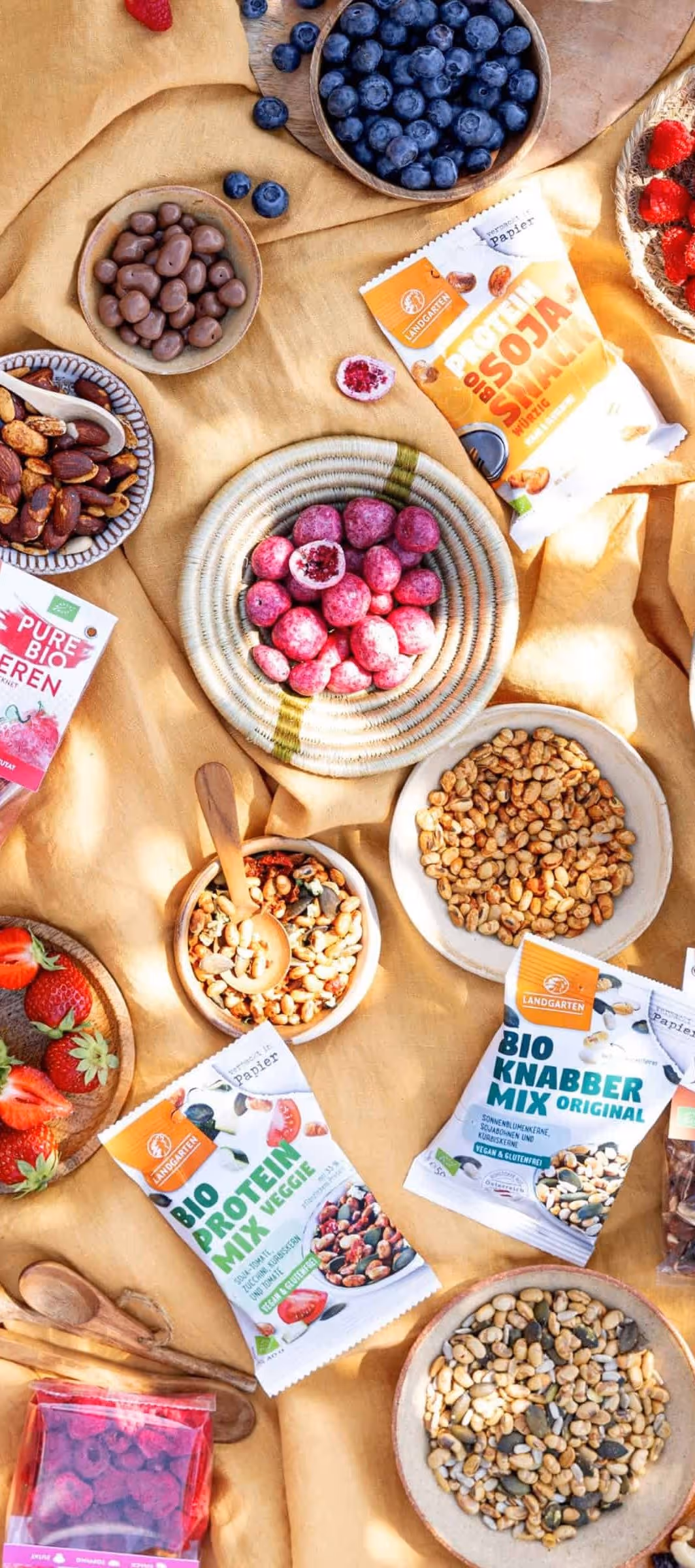 Assorted snacks including blueberries, strawberries, nuts, and protein mix packets on yellow fabric.
