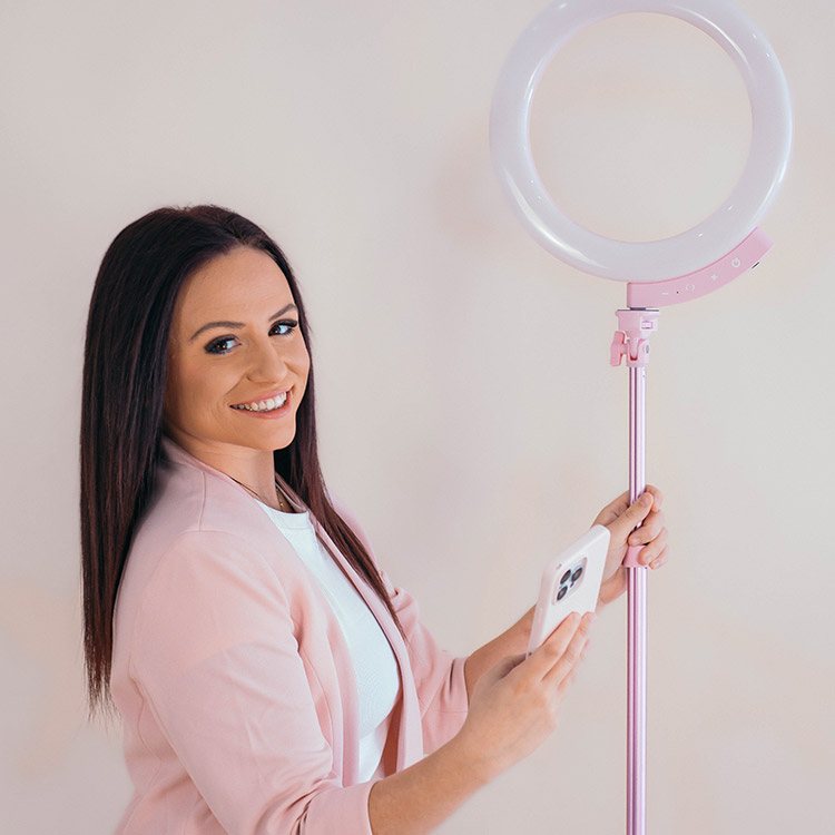 A team member from The Social Circle holding a smartphone beside a pink ring light used for content creation