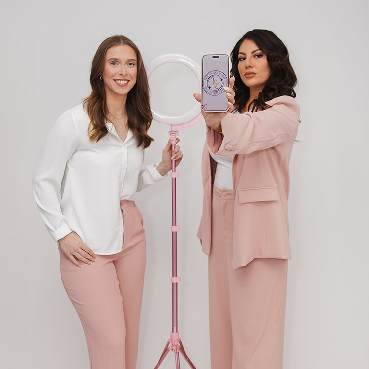 Natalie and a team member from The Social Circle posing beside a ring light while showcasing social media branding on a smartphone