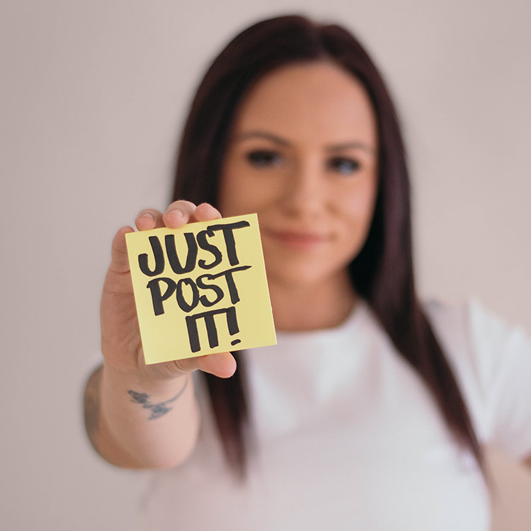 A team member from The Social Circle holding a sticky note that says “Just Post It!” toward the camera