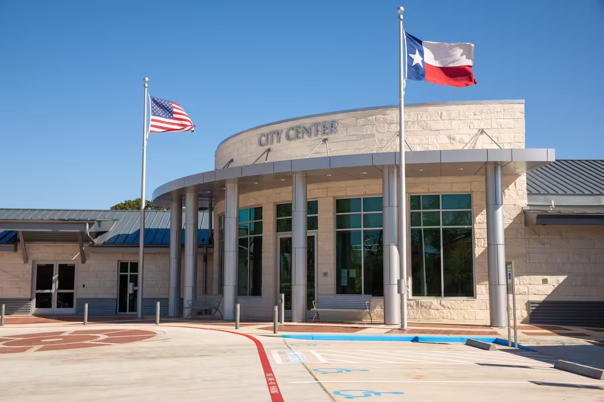 City Center building with Texas and US flags flying on flagpoles outside under blue sky.