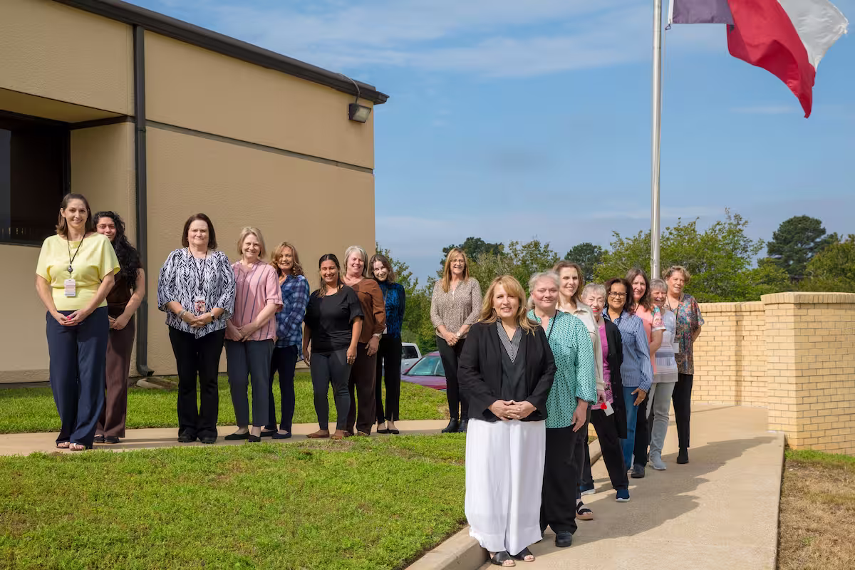 A group of women standing outside near a building and flagpole under a blue sky.