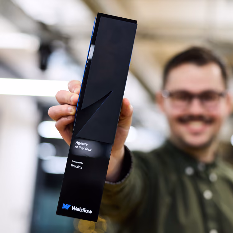 Person holding a black Webflow Agency of the Year trophy awarded to Parallax with a blurred background.