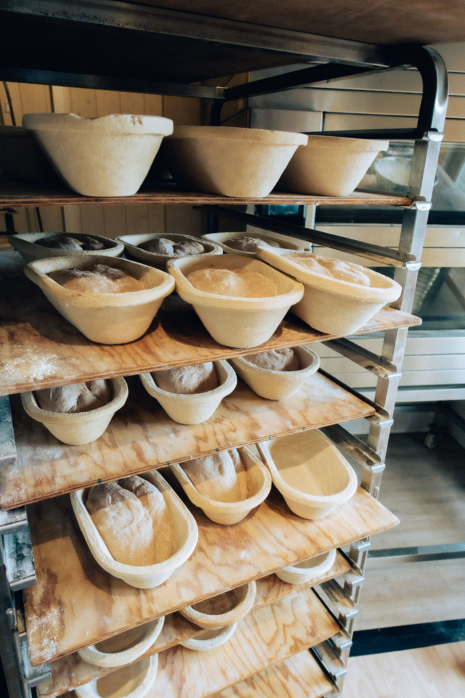 Gestapelte Brotteigformen mit Teig in einer Bäckerei auf Holzregalen.