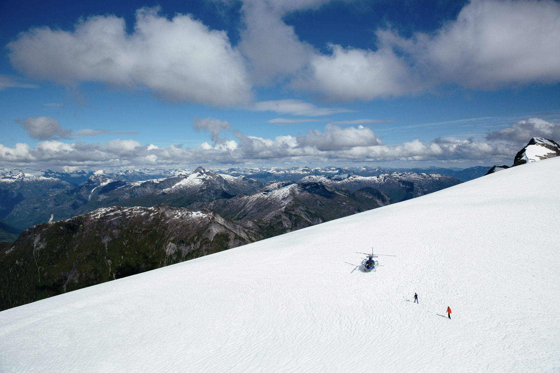 A helicopter parked on an alpine snowfield above the British Columbia coast range during a Nimmo Bay heli-adventure