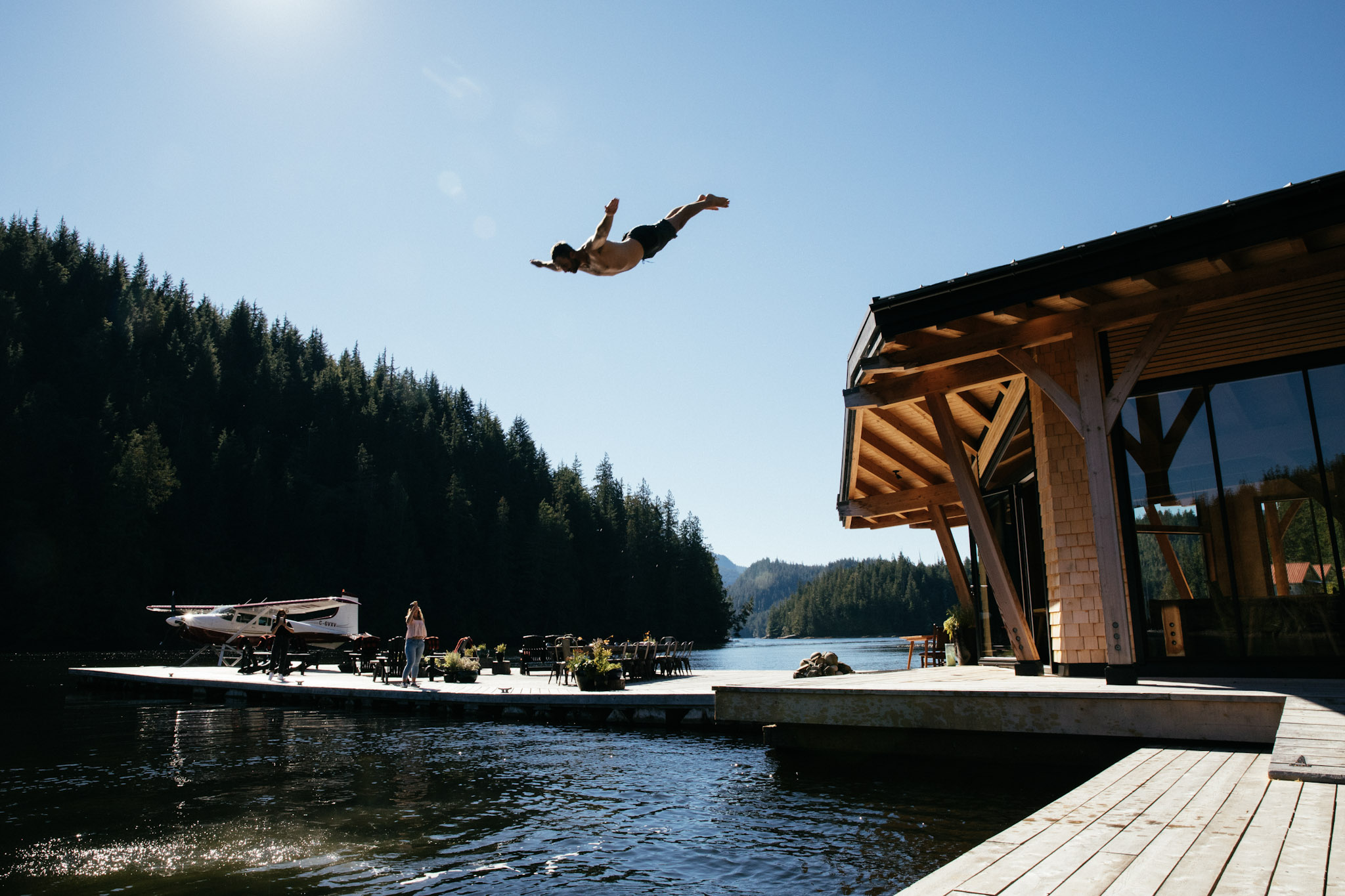 A guest dives from the lodge deck into the bay at Nimmo Bay, a floatplane moored at the dock behind