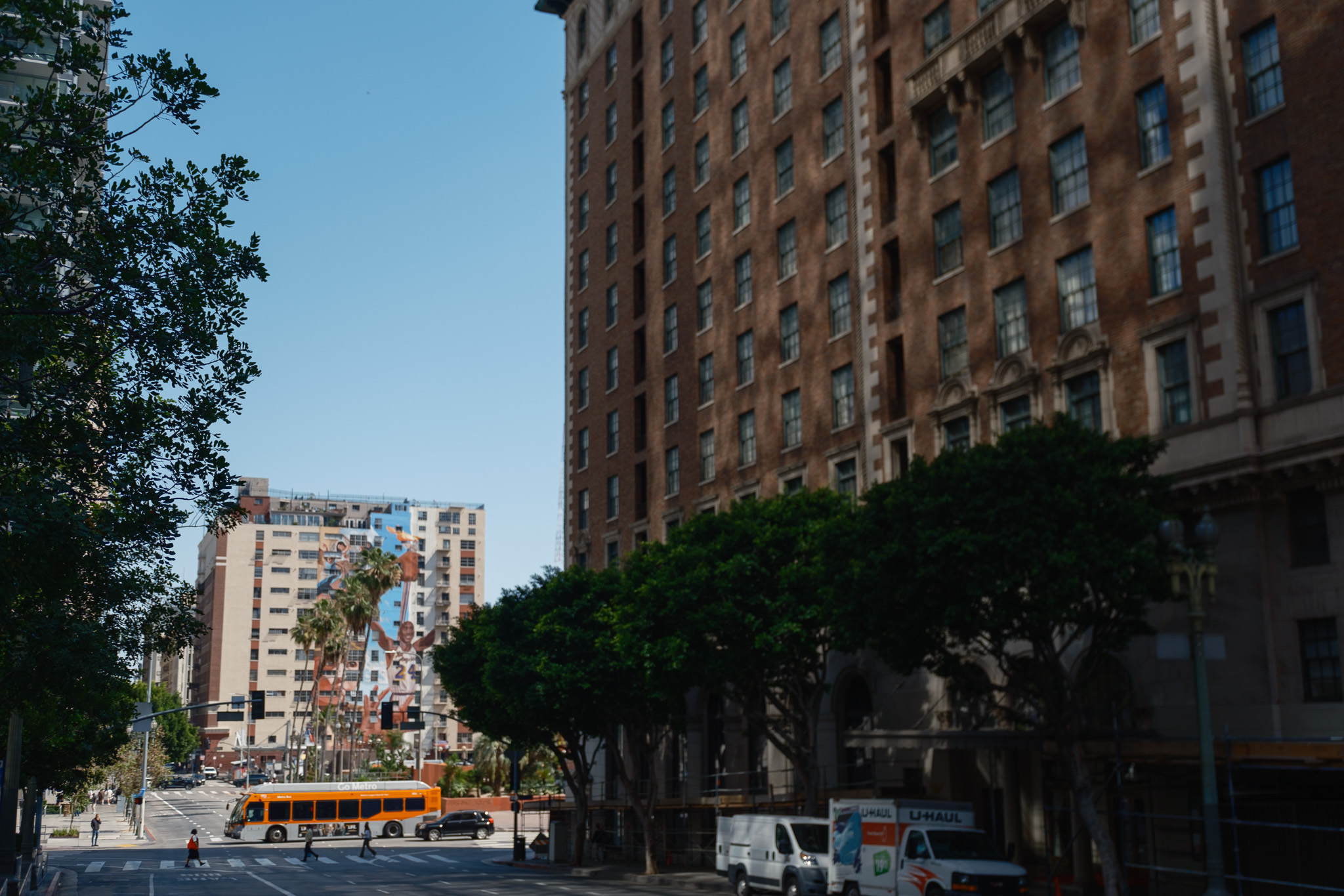 Downtown LA (DTLA) cultural walk, brick apartment building surrounded by trees, and mural with Kobe Bryant in the distance.