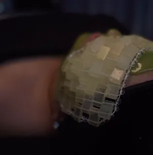 Close-up of a fabric with a grid of shiny, reflective sequins attached, against a dark background.