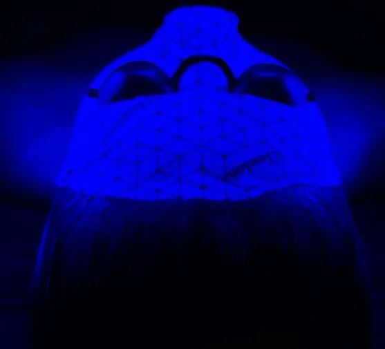 Person wearing a white geometric-patterned face mask and protective goggles under blue light.