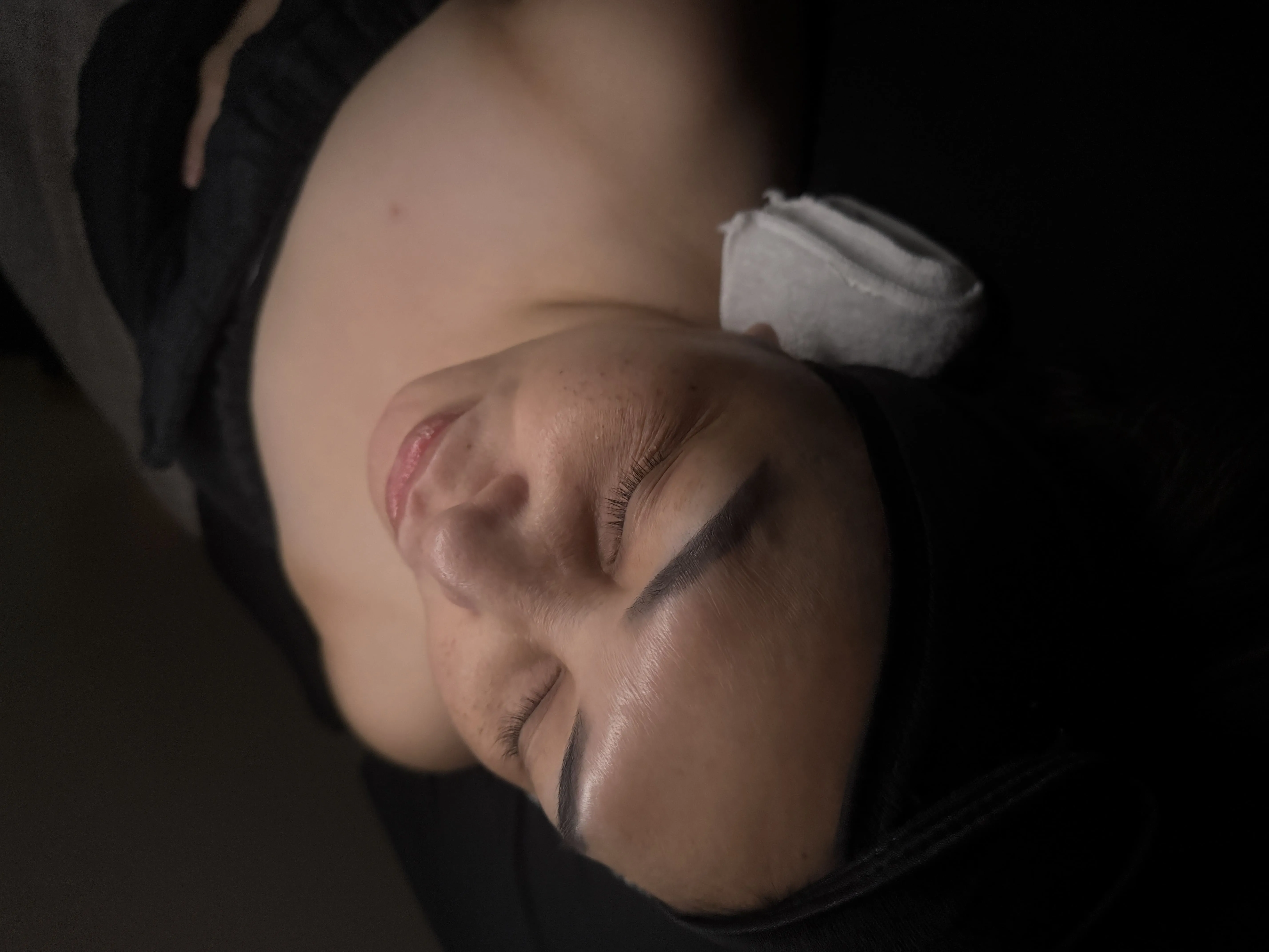 Close-up of a woman lying down with her eyes closed and a towel supporting her head.