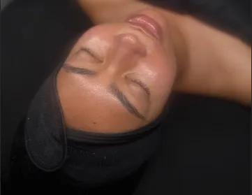 Close-up of a person with eyes closed wearing a black headband, lying down on a black surface.