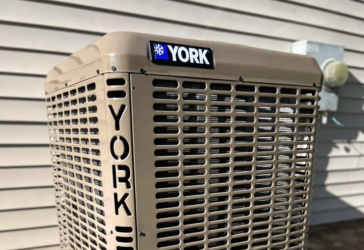 Beige York brand air conditioning unit installed outside a house with horizontal siding.