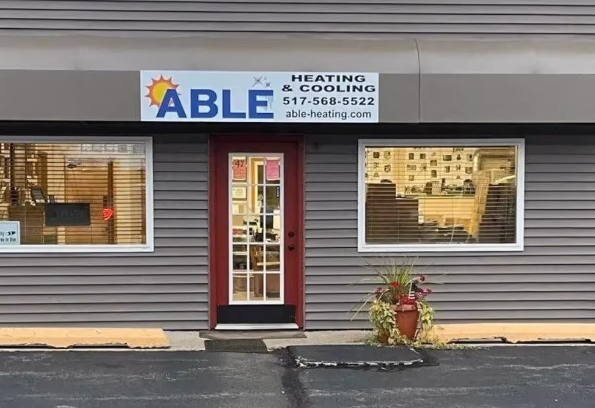 Gray building facade with a red door and sign reading Able Heating & Cooling with contact details.