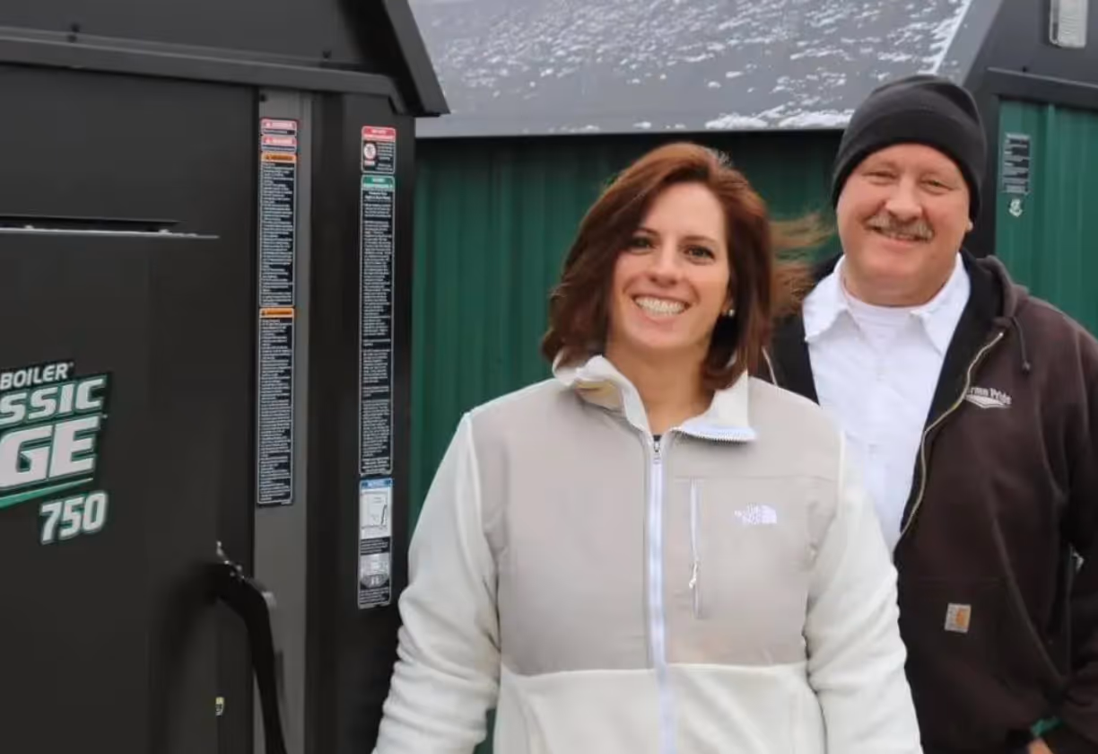 Smiling woman in light jacket and man in dark jacket and beanie stand outside near green building.
