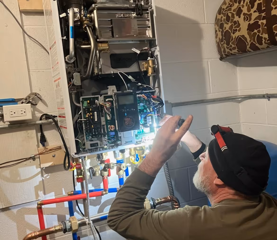 Technician inspecting the inside of a wall-mounted boiler unit with a flashlight.