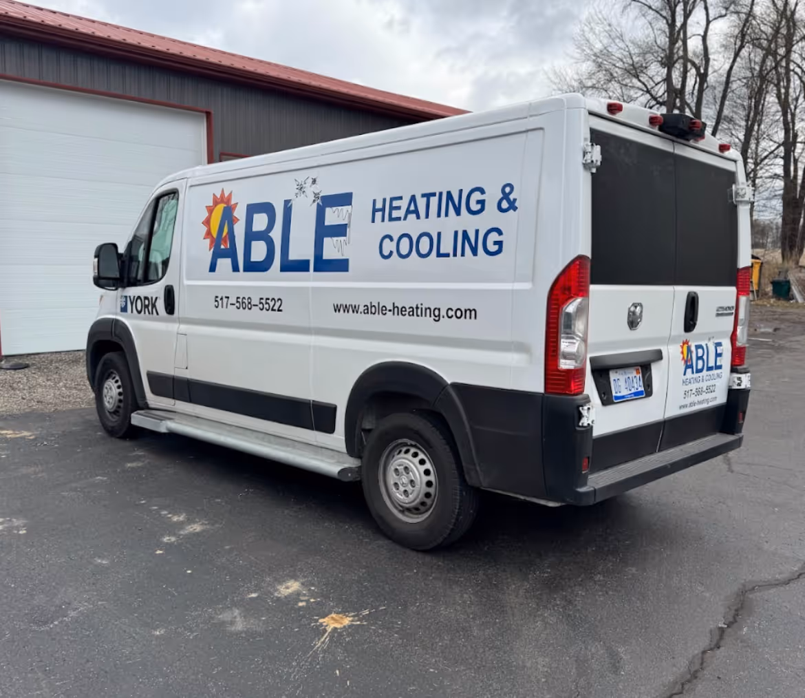 White van with Able Heating & Cooling branding, phone number, and website parked by a building.