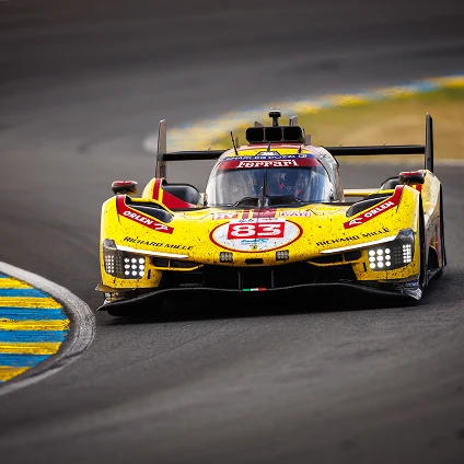 Yellow Ferrari race car number 83 on a curved race track with blue and yellow curb markings.
