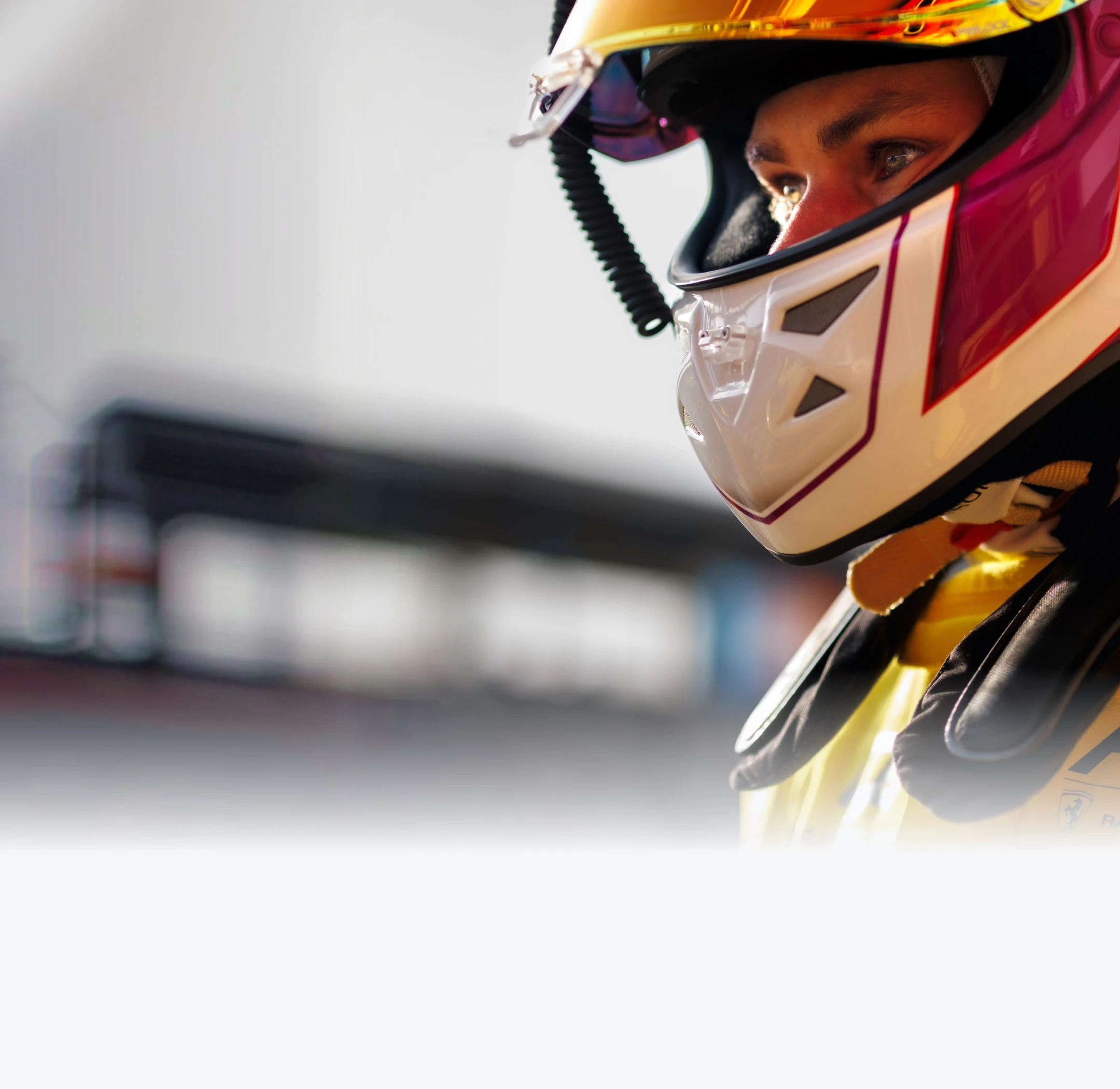 Close-up of a race car driver wearing a yellow and red helmet and racing gear, looking intently to the side.