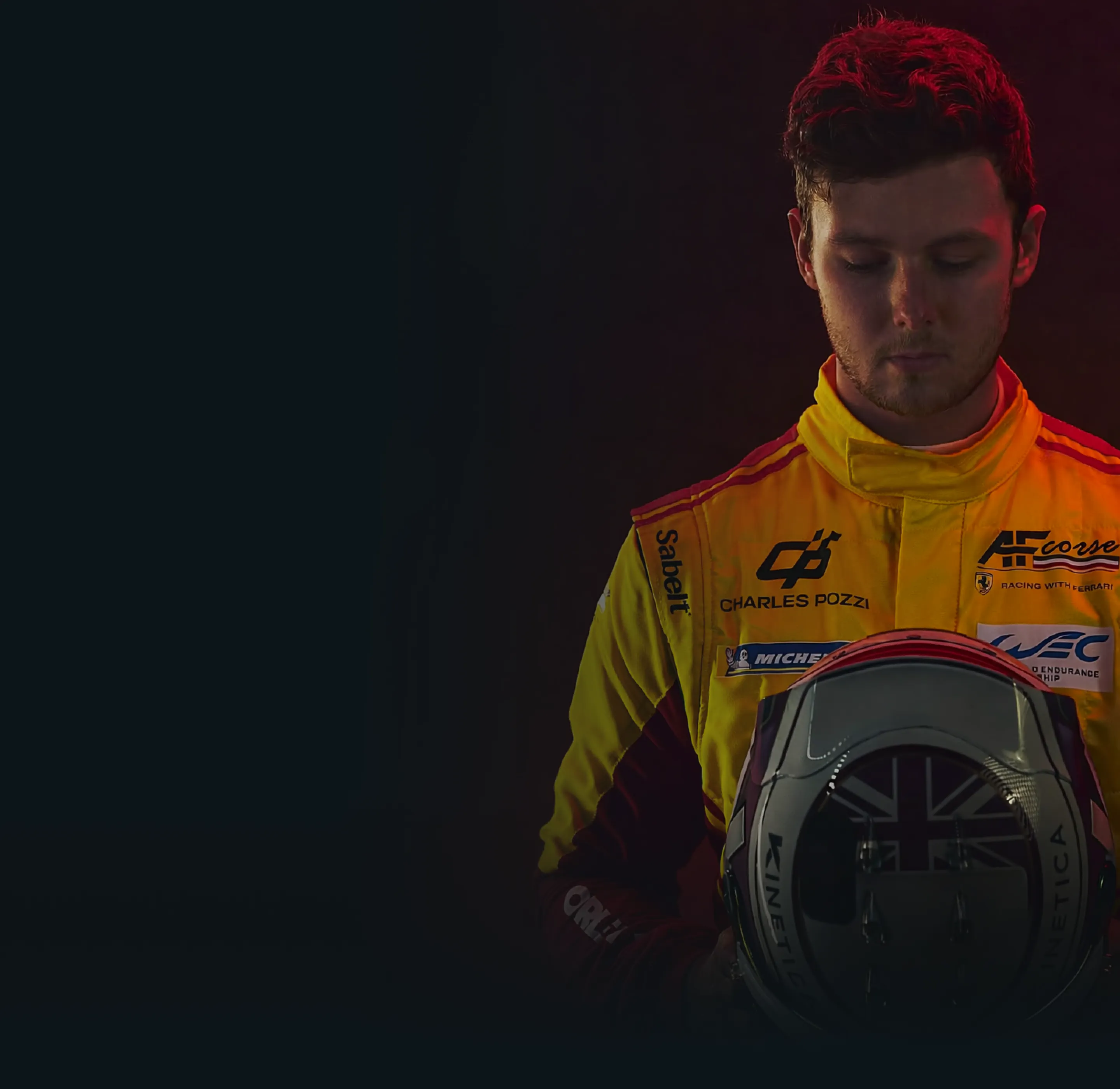 Race car driver in a yellow racing suit holding a helmet with a British flag design.