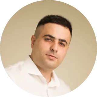 Man with short dark hair wearing a white shirt against a beige background.