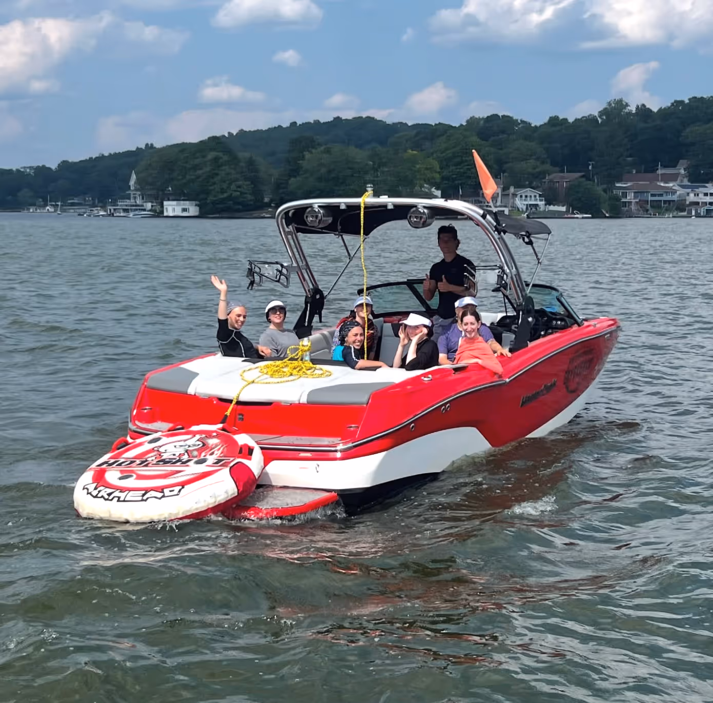 Group of young adults enjoying a boat ride on turquoise waters with city skyline and Ferris wheel in the background.