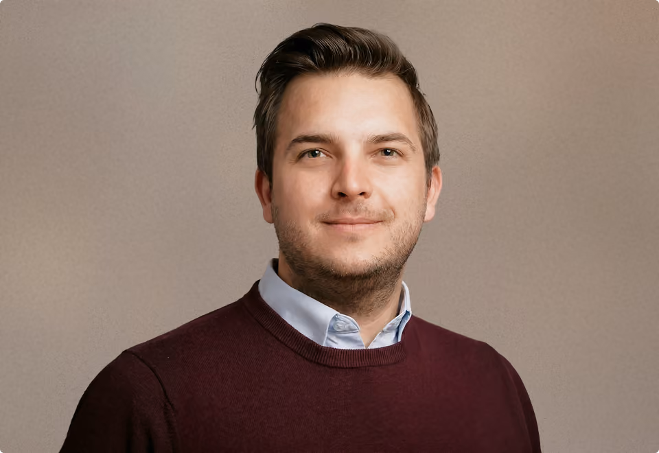 Porträt eines Mannes mit dunklem Pullover und hellem Hemd vor grauem Hintergrund