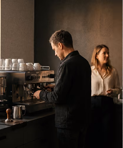 Mann bedient Espressomaschine in Café, Frau wartet im Hintergrund