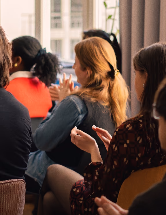 Mehrere Frauen sitzen zusammen und unterhalten sich in einem hellen Büro mit Blick auf Stadtgebäude.