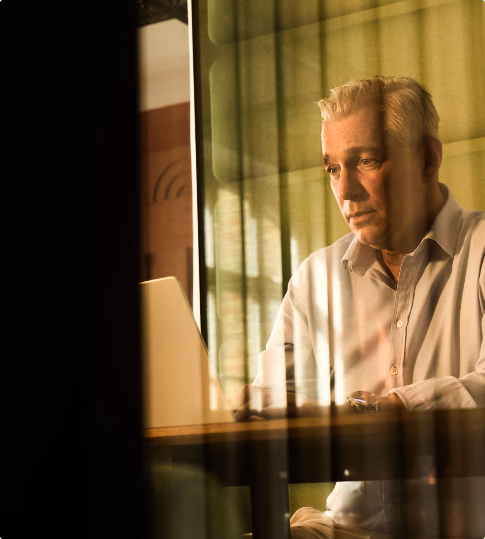Älterer Mann in weißem Hemd sitzt nachdenklich am Schreibtisch vor Laptop