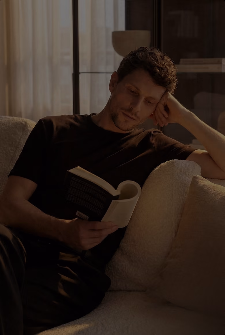Mann sitzt auf Sofa und liest konzentriert ein Buch im warmen Licht
