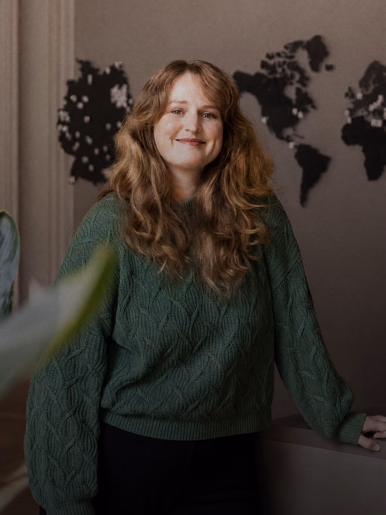 Frau mit langen braunen Wellen trägt grünen Pullover vor Weltkarte