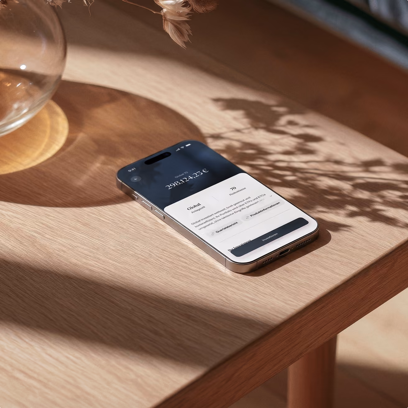 iPhone mit Banking-App auf Holztisch neben Glas, Sonnenlicht wirft Schatten