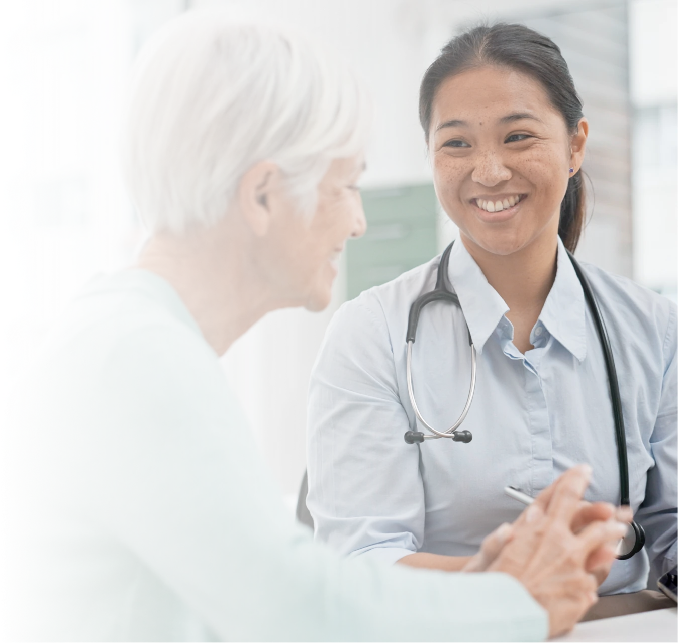 Smiling female doctor with stethoscope talking to an elderly woman in a medical office.