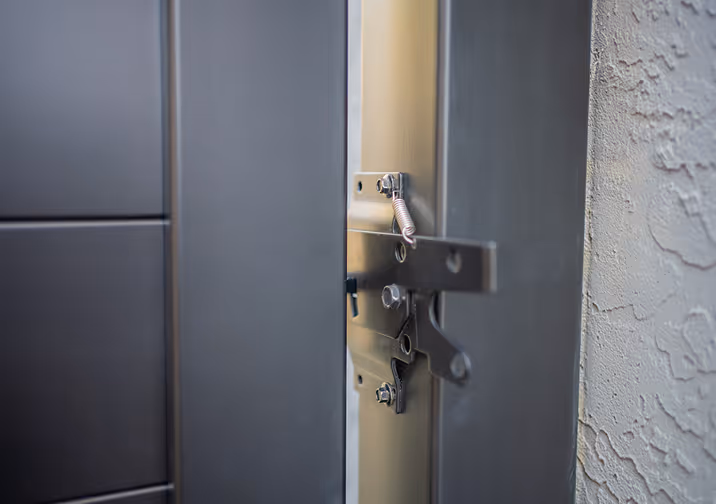 Close-up of metal latch mechanism on a partially open door with textured wall in the background.