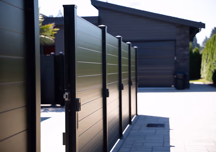 Black metal gate panels forming a secure fence in front of a modern house with a driveway.