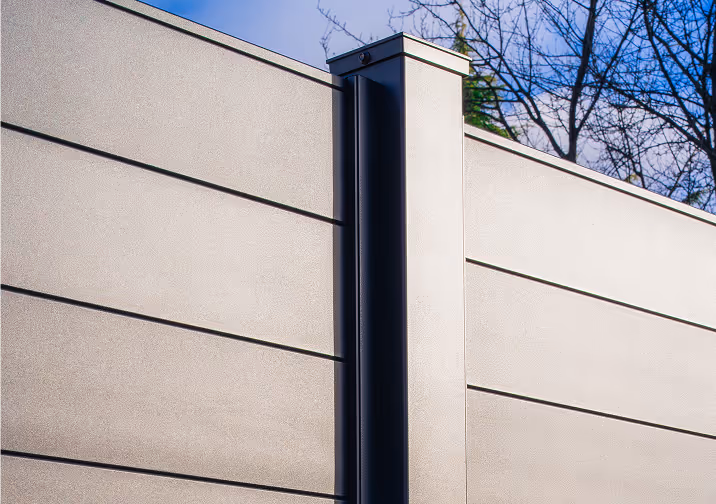 Close-up of a modern grey horizontal panel fence with a vertical black support post and bare tree branches in the background.