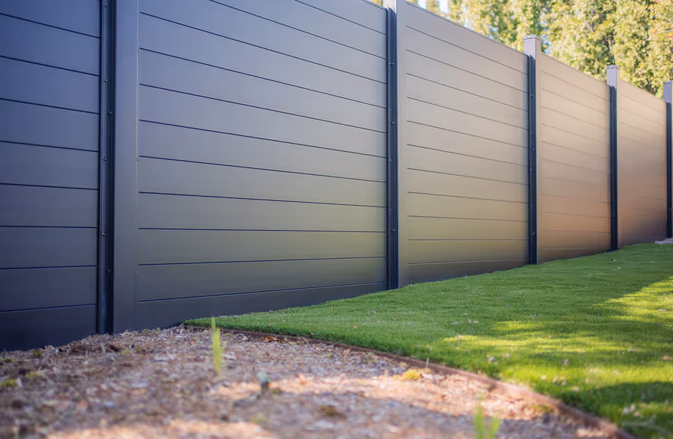 Long metal privacy fence with horizontal panels bordering a lawn and garden bed.