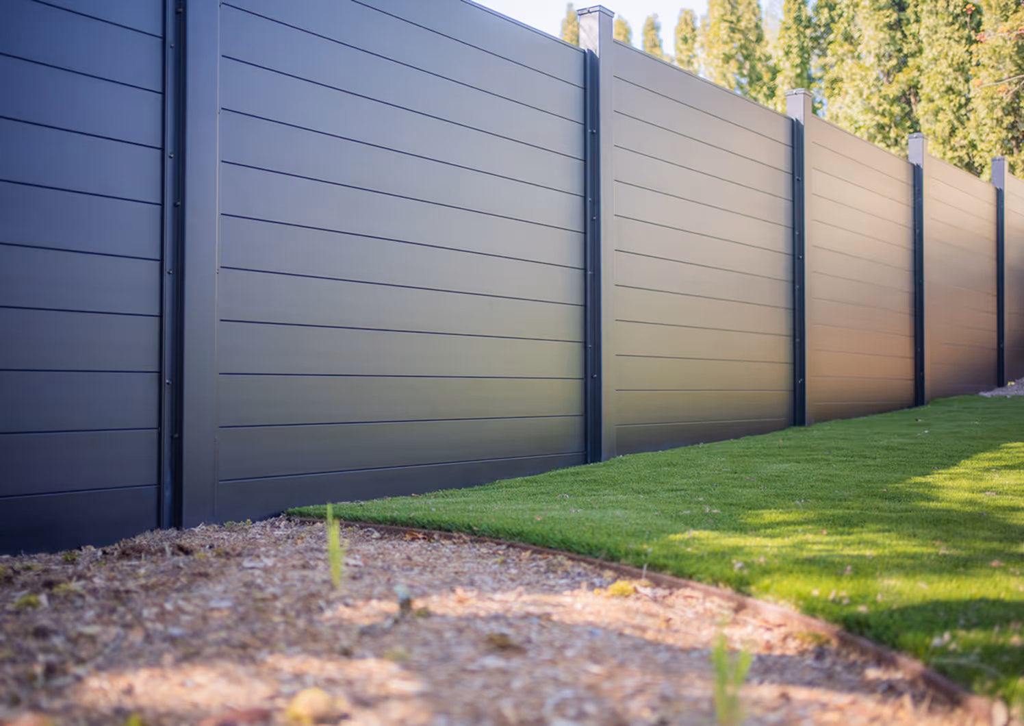 Modern dark gray metal fence panels installed alongside a neatly trimmed lawn and a mulched garden bed.