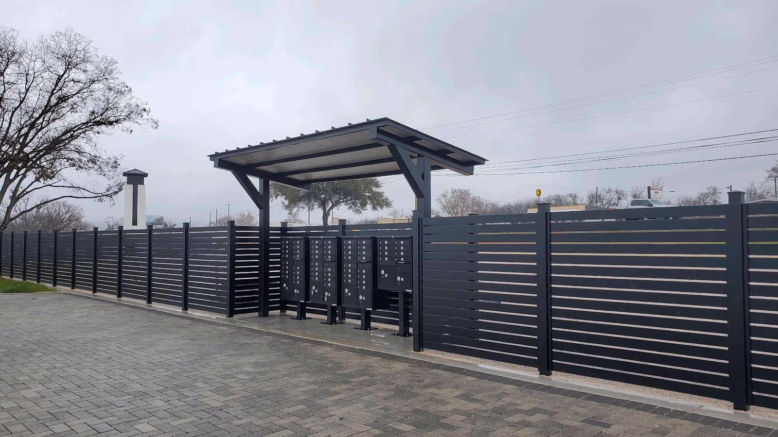 Modern horizontal aluminum fence with semi-privacy panels surrounding covered community mailboxes in an outdoor setting.