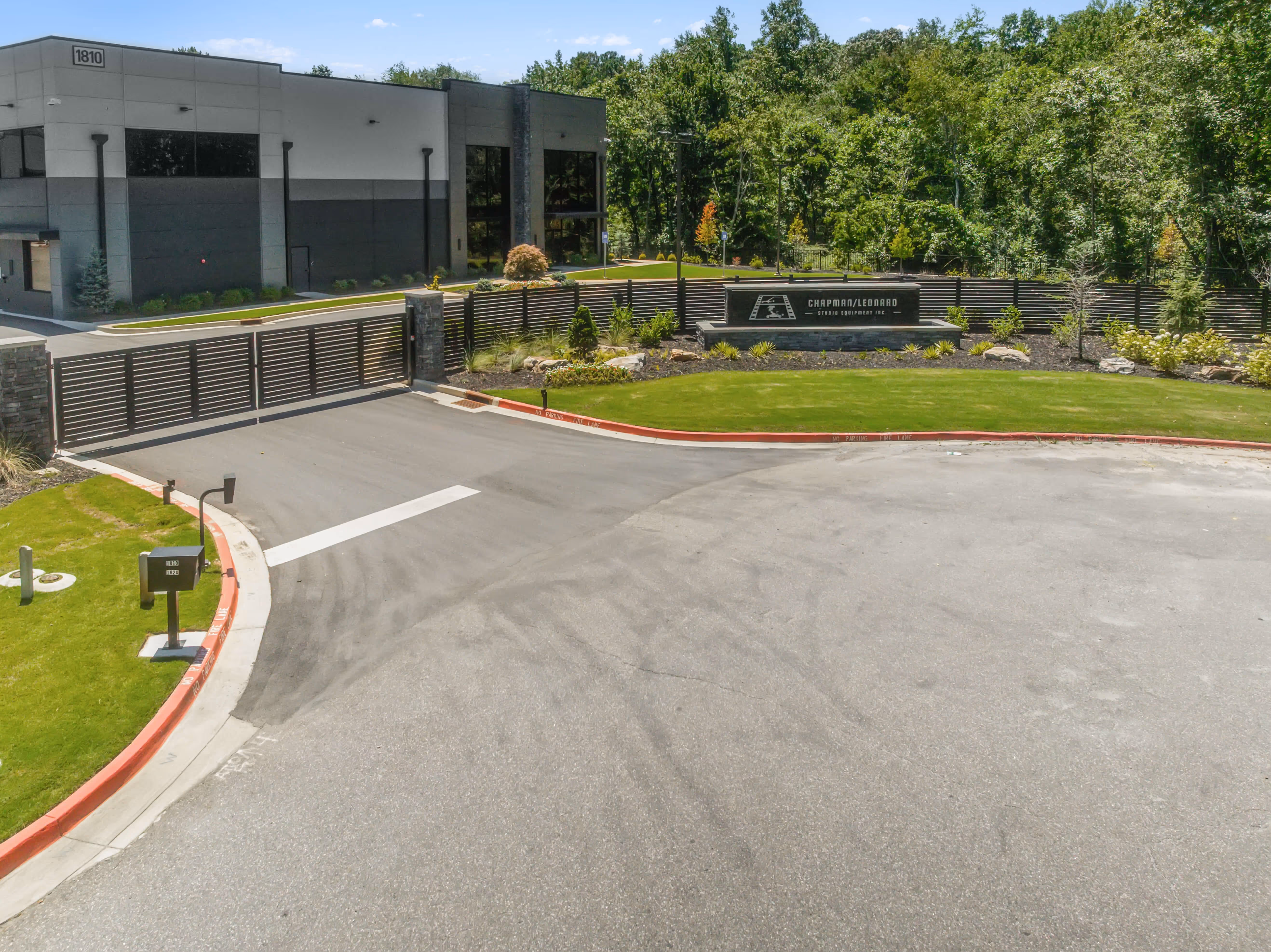 Entrance to a commercial building with a closed aluminum double swing driveway gate and landscaped greenery.