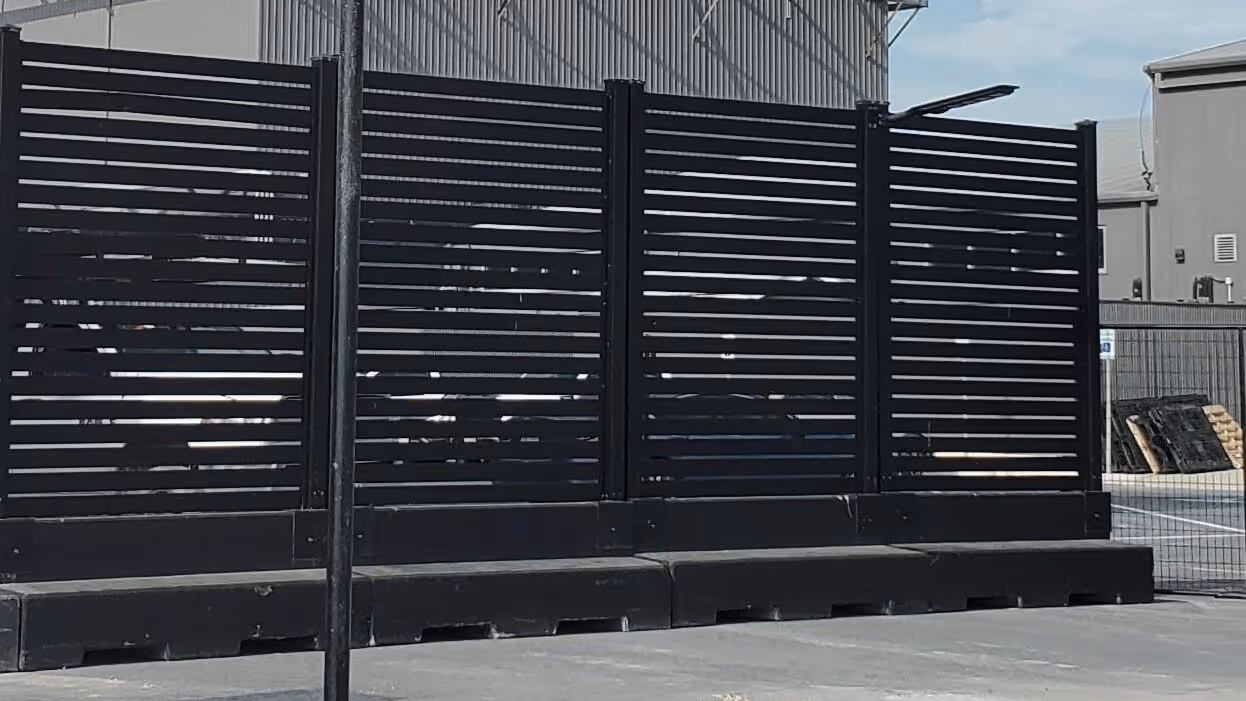 Black horizontal slat aluminum fence panels installed outdoors with industrial buildings in the background.