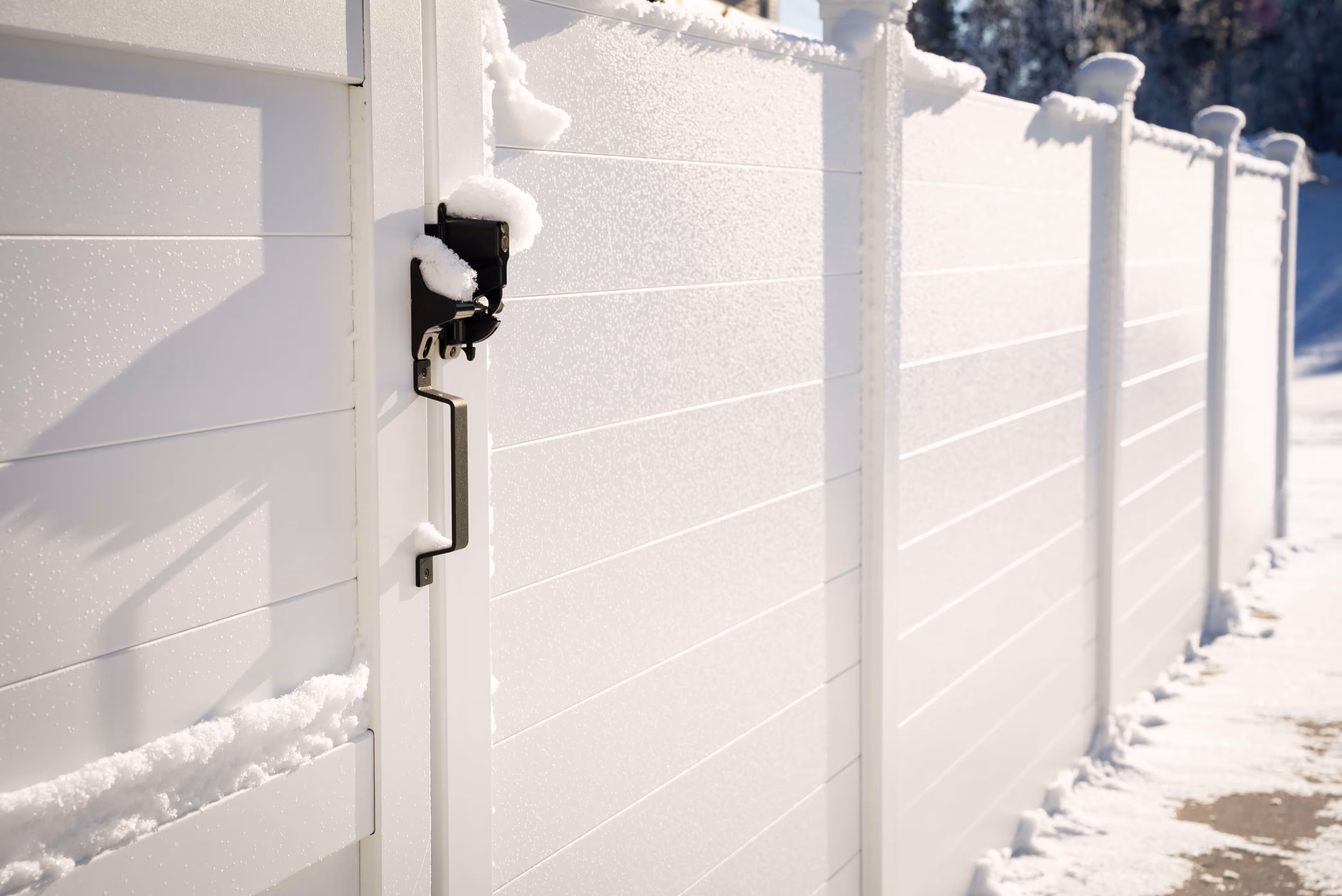 White aluminum privacy fence and gate dusted with snow on a sunny winter day.