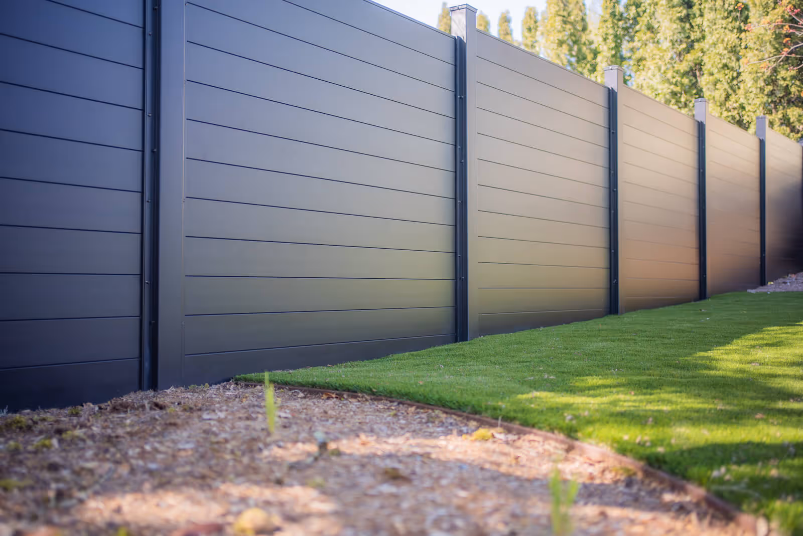 Black modern horizontal aluminum privacy fence along a landscaped yard with green grass and mulch.