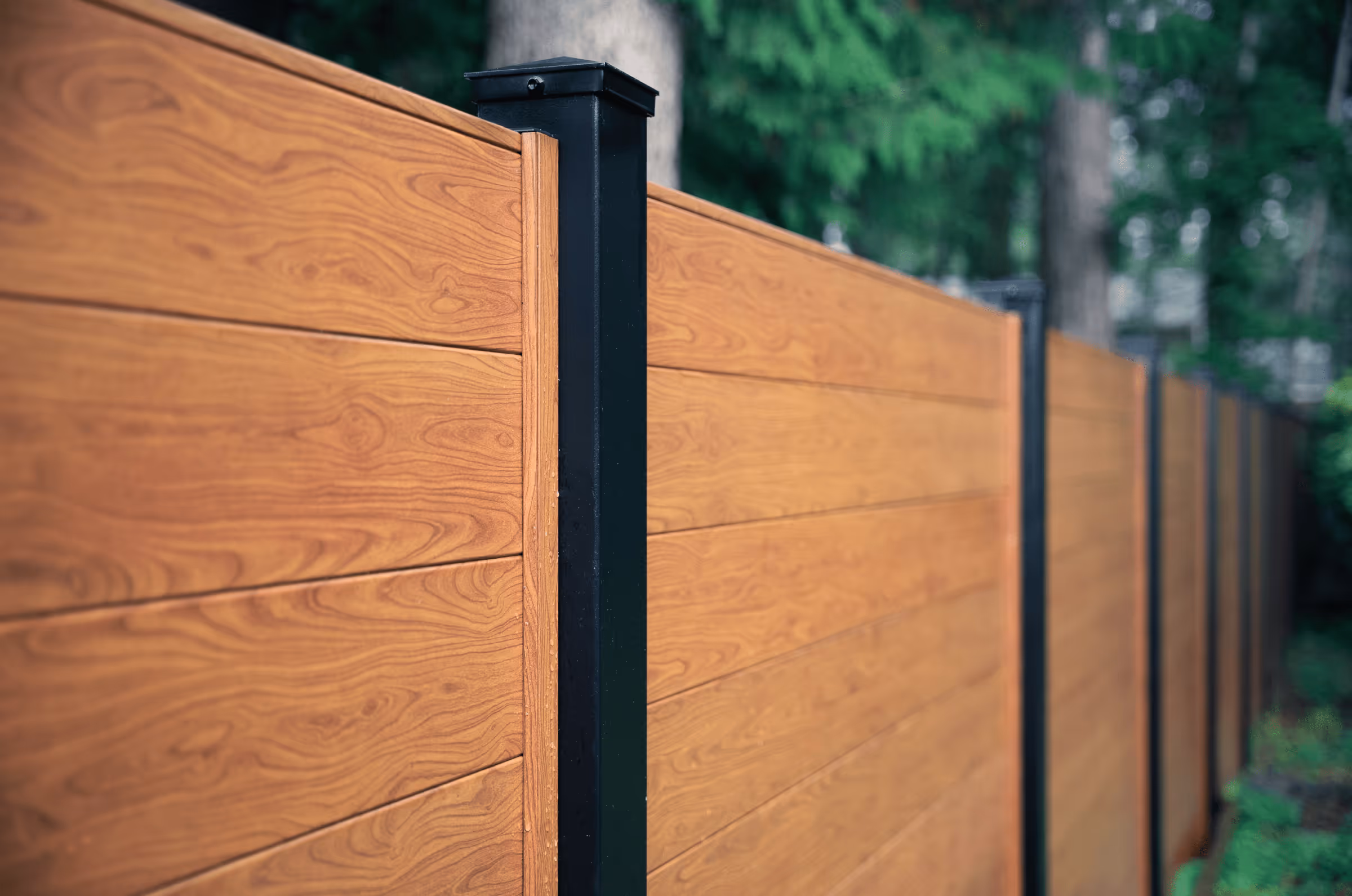 Close-up view of a horizontal wood-grain aluminum privacy fence with black posts in an outdoor setting.