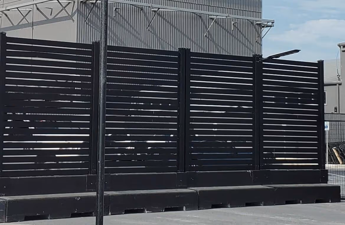 Black aluminum privacy fence panels with horizontal slats in an industrial outdoor setting.