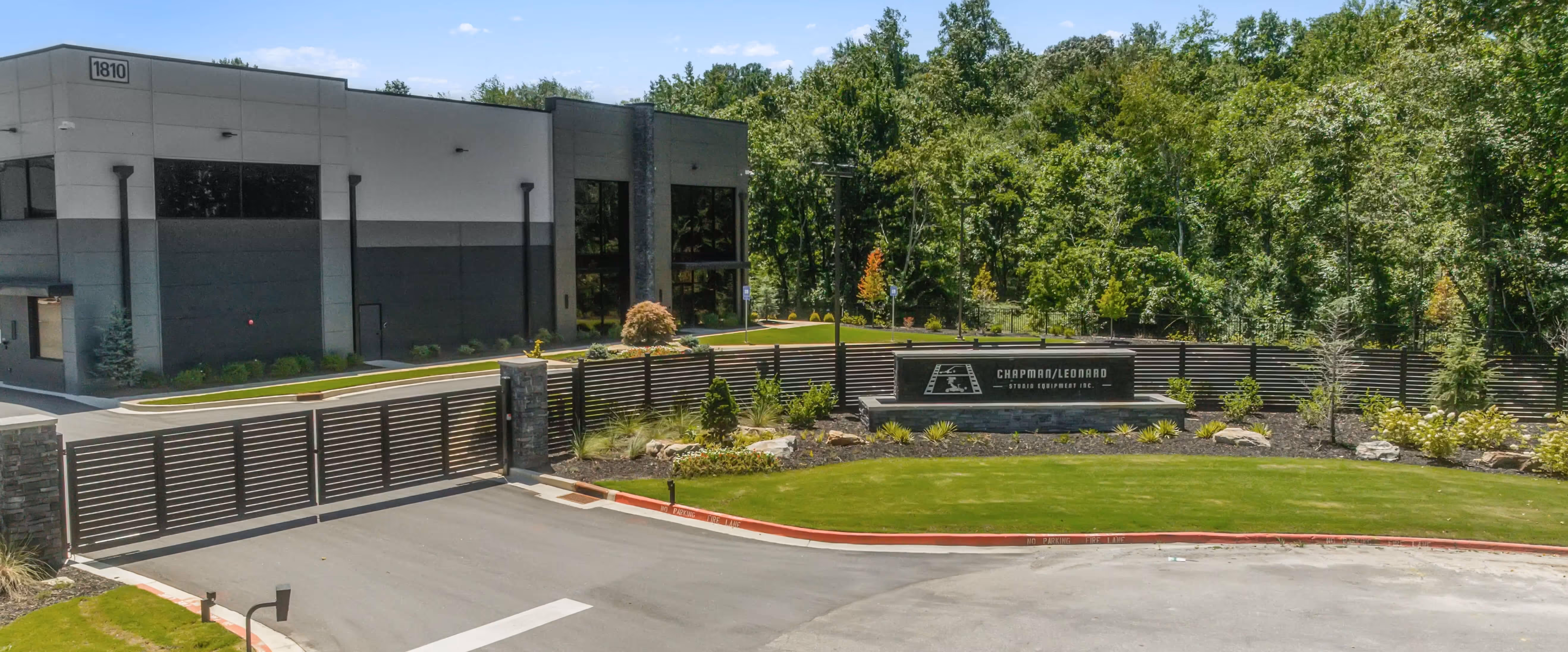 Modern commercial building behind a horizontal slat aluminum double swing driveway gate with landscaped grass and trees.