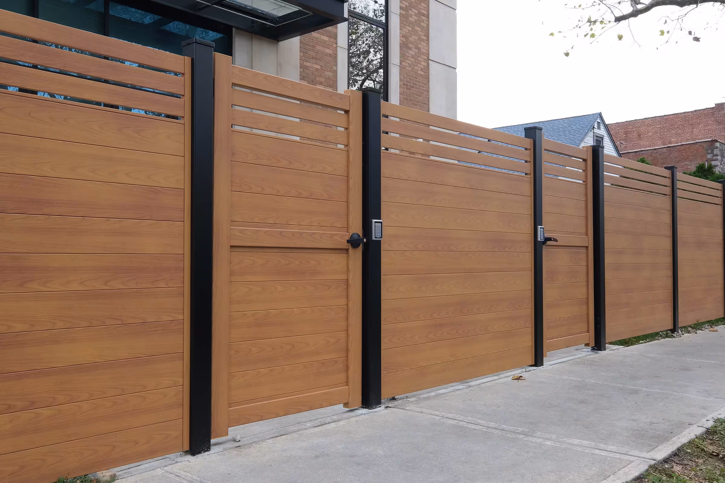 Modern horizontal wooden privacy fence with black vertical posts and two gates, each equipped with a keypad lock and handle.