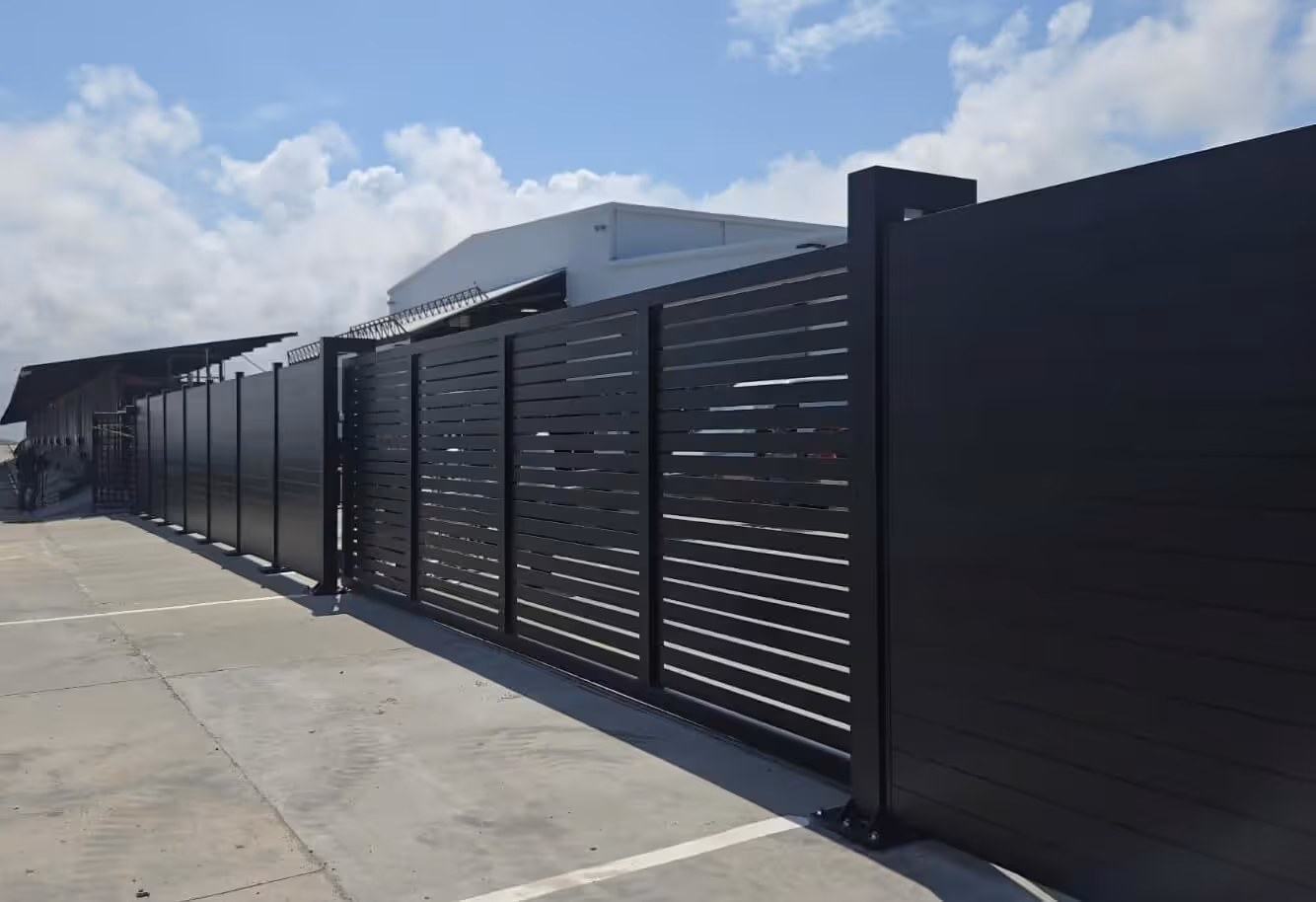 Long modern black aluminum driveway gate with horizontal slats under a partly cloudy sky.